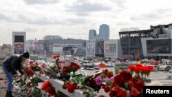 Russia - A woman lays flowers on the roadside in front of the burnt-out Crocus City Hall on the outskirts of Moscow, March 26, 2024. 