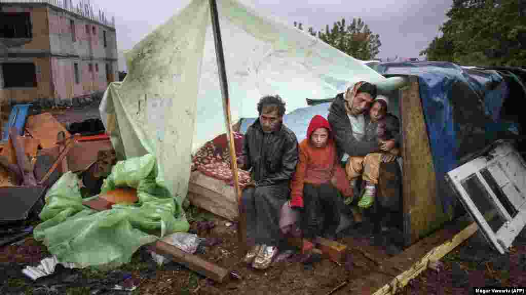 A Roma family of Turkish origin sits under an improvised shelter to protect from heavy rain in the coastal Romanian town of Eforie Sud on September 30. Romanian authorities evicted around 100 Roma from the town, near the Black Sea coast, without providing them with alternative housing. (AFP/Mugur Varzariu)