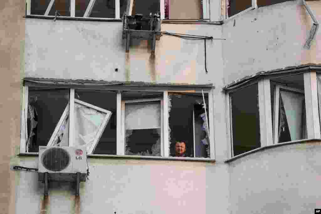 A man looks from a window of a residential multistory building damaged after a Russian drone strike on Kyiv.