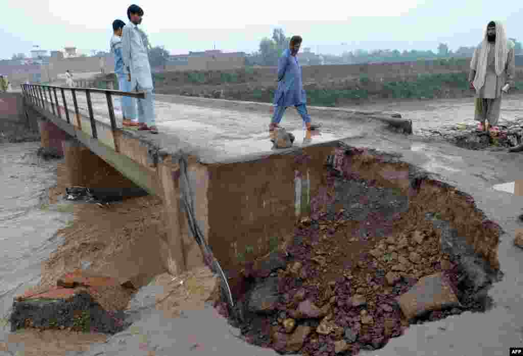 Pakistanis walk on a damaged bridge over a flooded river in Peshawar.