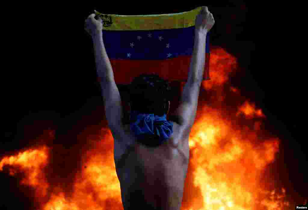 Un protestatar afișează steagul național pe fundalul incendierii unui oficiu bancar în timpul unui miting împotriva președintelui Venezuelei, Nicolas Maduro. Caracas, 12 iunie 2017. (Reuters/ Carlos Garcia Rawlins)