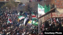 Syrian protesters wave flags, including the green-white-red one of Chechnya Ichkeria (center), in Ras al-Ain on February 6.