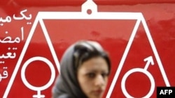 A woman walks past a banner reading "one million signatures to change the biased laws" in Tehran.