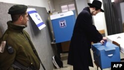 An Israeli border policeman stands guard as a man casts his ballot in Jerusalem for Israeli parliamentary elections.