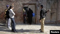 A policeman stands guard as female polio workers wait to administer polio vaccines to children in Lahore, Pakistan, on December 20.