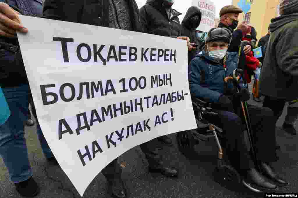 Мужчина в инвалидном кресле на митинге в Алматы. Надпись на плакате призывает президента Казахстана Касым-Жомарта Токаева услышать требования 100 тысяч человек. В августе инициативная группа по созданию Демократической партии во главе с Жанболатом Мамаем заявила, что в администрацию президента Токаева было передано &laquo;около 100 тысяч заявлений&raquo; с призывом объявить кредитную амнистию.