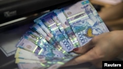 Коммерциялық банктегі кассир ақша банкноттарын тексеріп жатыр. 