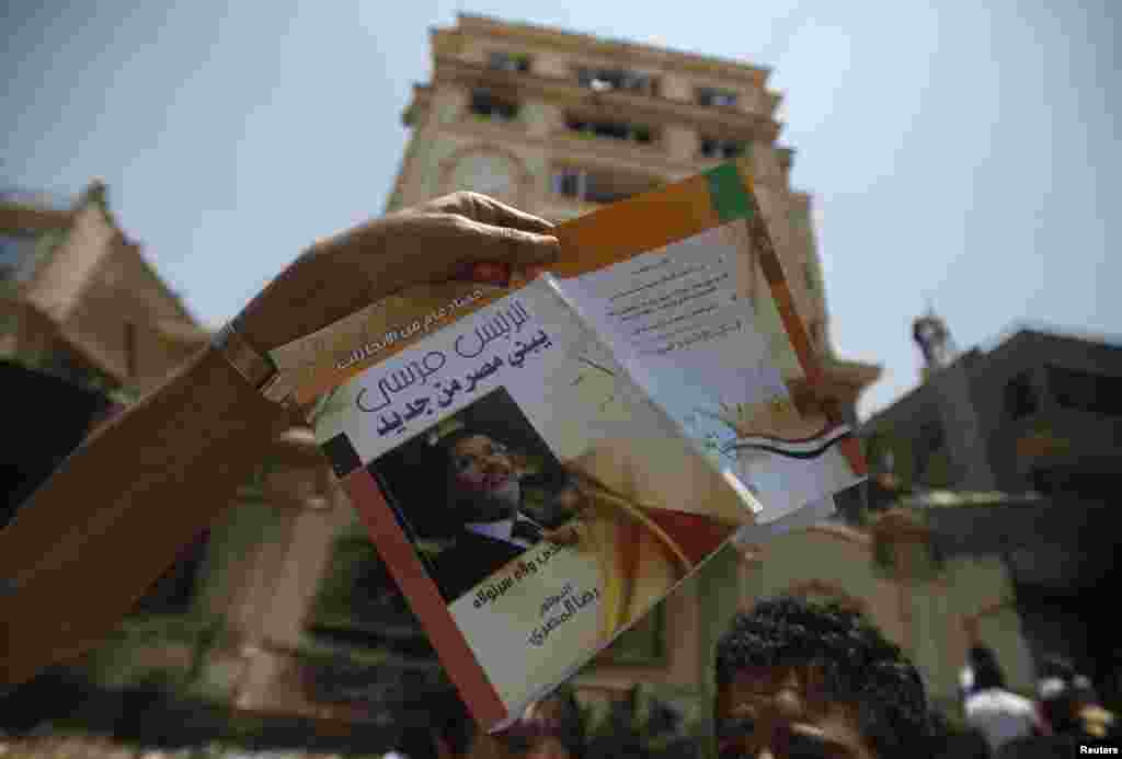 A protester holds up a book titled &quot;President Morsi Is Building A New Egypt&quot; in front of the Muslim Brotherhood headquarters.