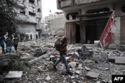 People carry salvaged items amid the rubble of buildings damaged during an Israeli air strike on the Bureij refugee camp in the central Gaza Strip on October 8.