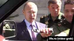 Russia President Vladimir Putin looks on, bemused, as the handle on the door of the armored SUV comes off in the hand of General Aleksandr Shevchenko, while the chief of the Russian Armed Forces General Staff, General Valery Gerasimov, looks on, appalled.