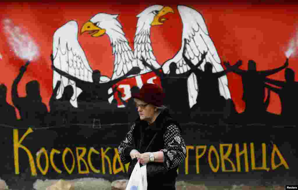 An ethnic Serb woman walks past a mural that includes part of the Serbian coat of arms in the northern part of Mitrovica.