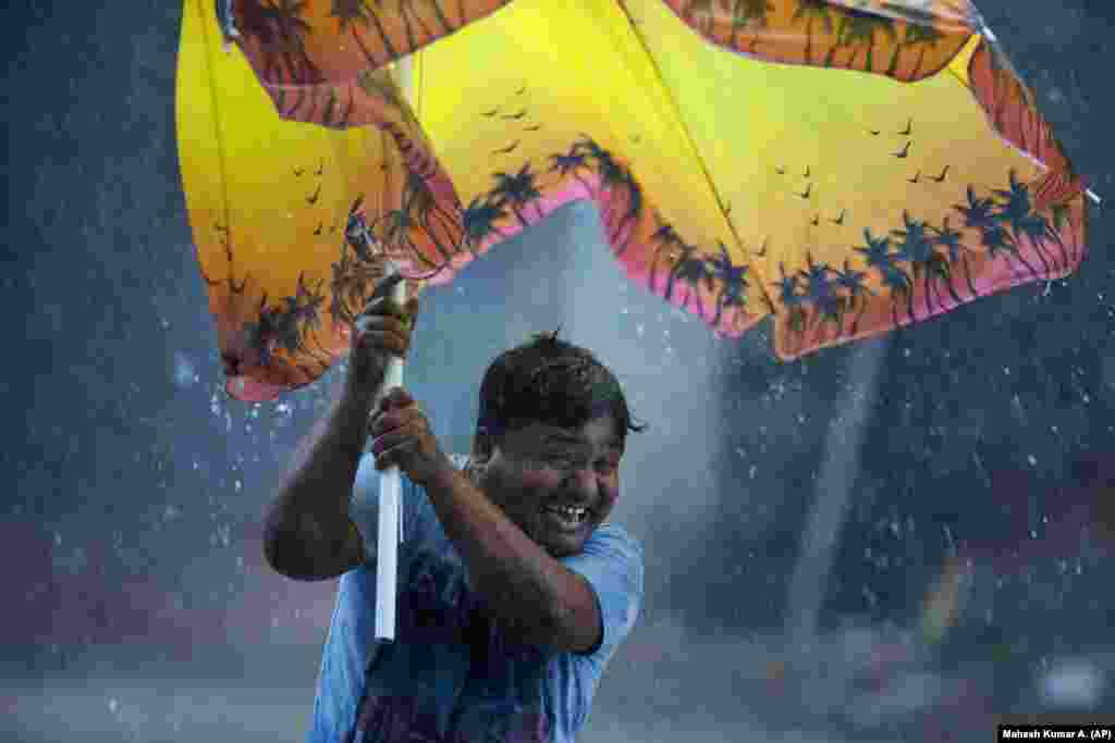 An Indian man reacts as he struggles to hold an umbrella against strong winds during a rain in Hyderabad. (AP/Mahesh Kumar A.)