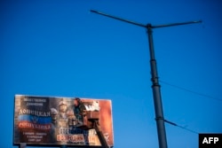 Рабочий клеит предвыборный плакат на бигборд в Макеевке, Донецкая область