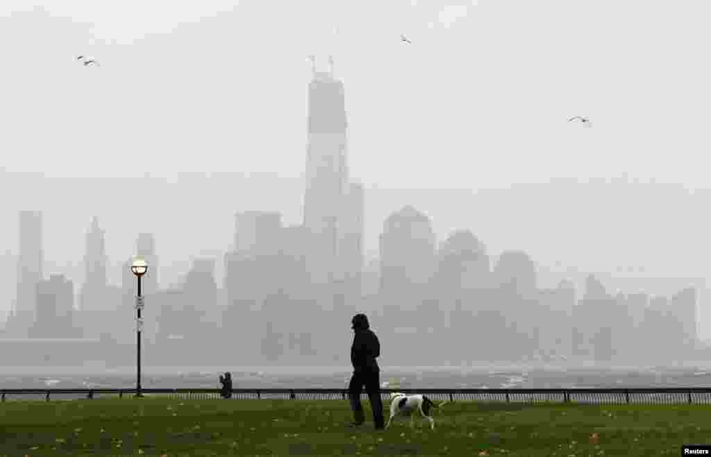 A person walks through a park along the Hudson River across from New York's Lower Manhattan as rain falls in Hoboken, New Jersey.