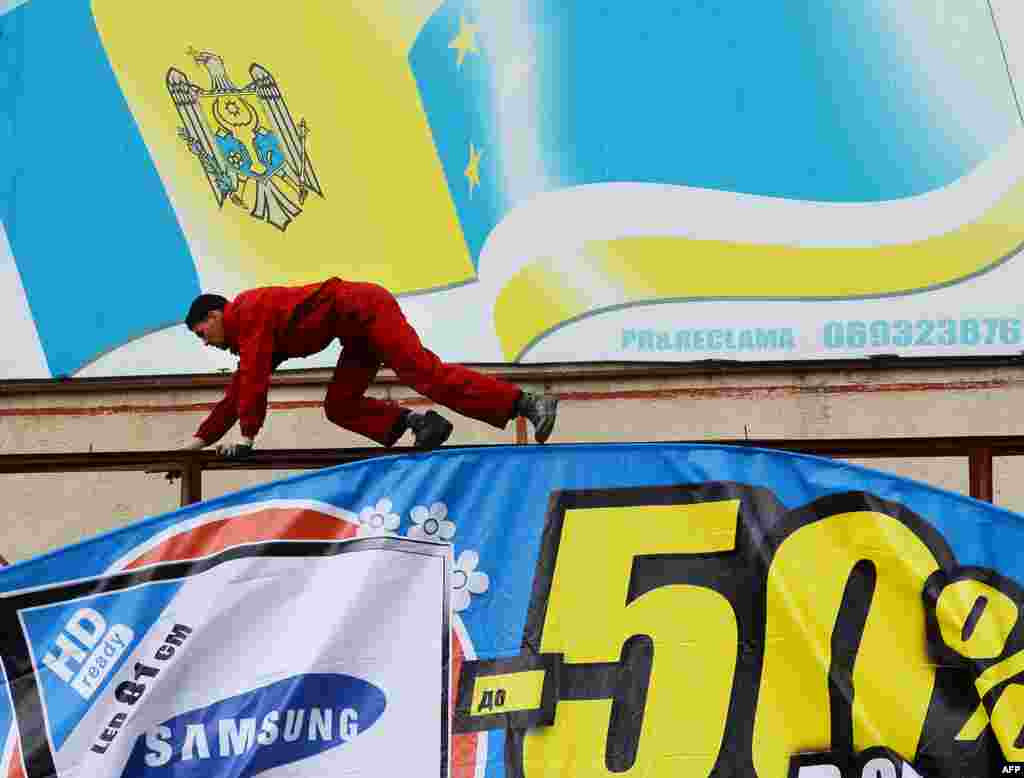 A worker installs a new billboard beneath the faded flags of Moldova and Gagauzia.