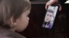 The 2-year-old daughter of imprisoned Belarusian blogger Ihar Losik looks at her father's photograph on the mobile phone of his wife, Darya Losik.