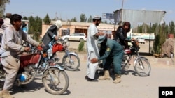 An Afghan security official checks people at a checkpost in Helmand.