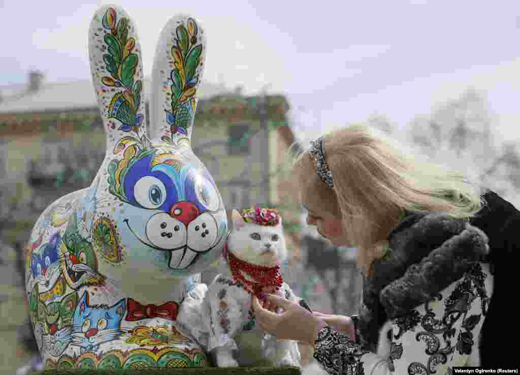 A woman dresses her cat before taking pictures near a painted Easter Bunny displayed in a square as part of Orthodox Easter celebrations in central Kyiv, Ukraine. (Reuters/Valentyn Ogirenko)