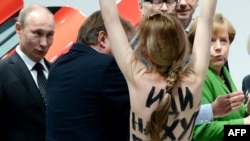 A topless demonstrator with a message on her back walks toward Russian President Vladimir Putin (left) and Chancellor Angela Merkel (right) during their visit to the industrial fair in Hannover on April 8.