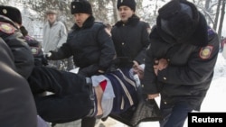Алматылық полицейлер демонстрантты ұстап әкетіп барады.