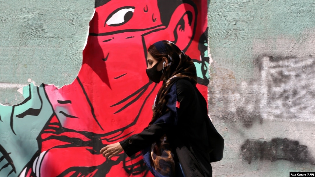 An Iranian woman wearing a protective mask walks past mask graffiti in Tehran.