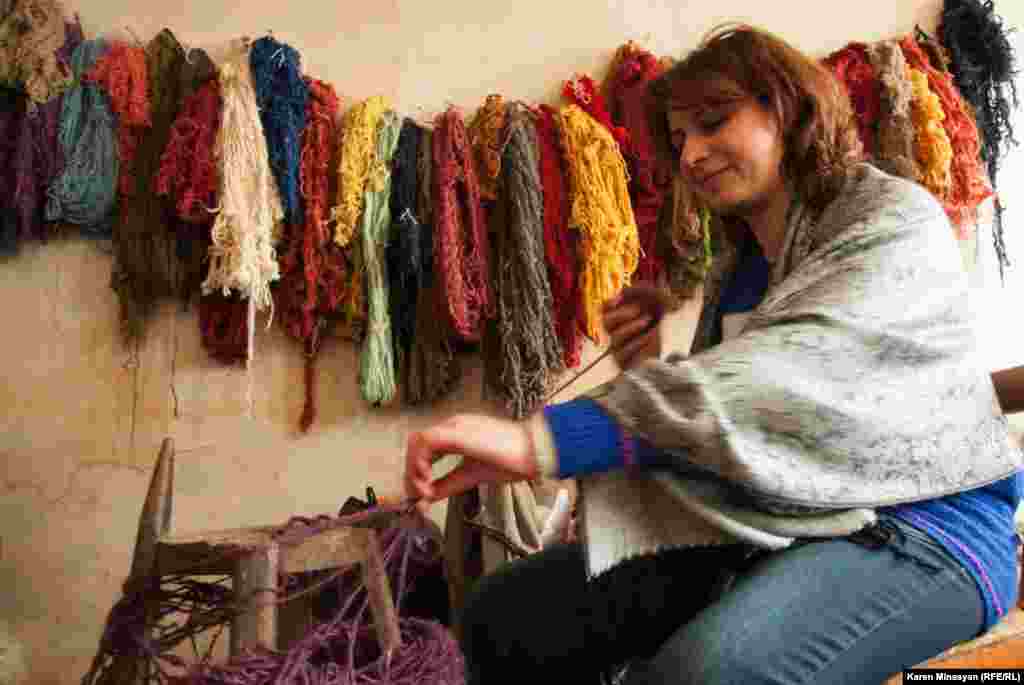 A woman gathers string to form a ball of yarn in front of a variety of colored thread.