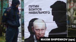 Imaginea unei toleranțe dispărute: polițist lângă un afiș care spune: «Putin se teme de Navalnîi», cu umbra acestuia deasupra lui Putin, în Kirov, 16 oct., 2013