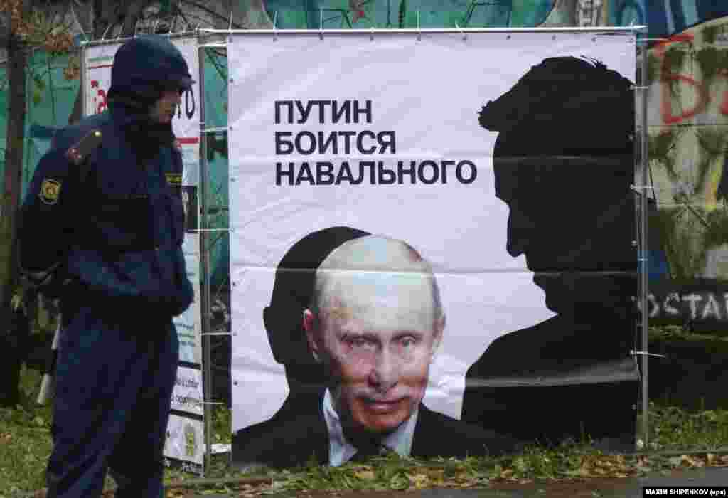 A police officer stands near a placard depicting Russian opposition leader and anticorruption blogger Aleksei Navalny's shadow (right) bending over President Vladimir Putin in Kirov. (epa/Maksim Shipenkov)