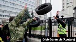 A man throws a tire at a security guard as protesters rally outside the Constitutional Court building, demanding the judges come out and explain the reasons for their ruling in Kyiv on October 30.