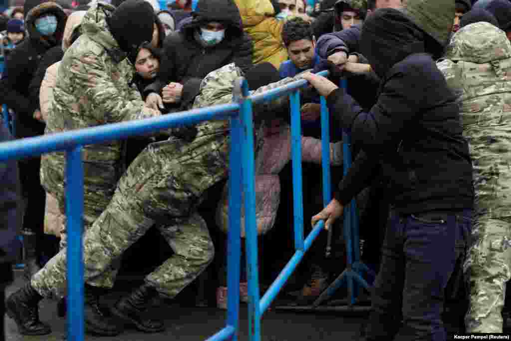 Belarusian servicemen hold a barrier as migrants jostle to receive food. The West has accused Lukashenka of &quot;weaponizing migration&quot; by bringing would-be migrants to Belarus and encouraging them to try to cross the border into Poland. Belarus has denied the accusation and has criticized the EU for not accepting the migrants.