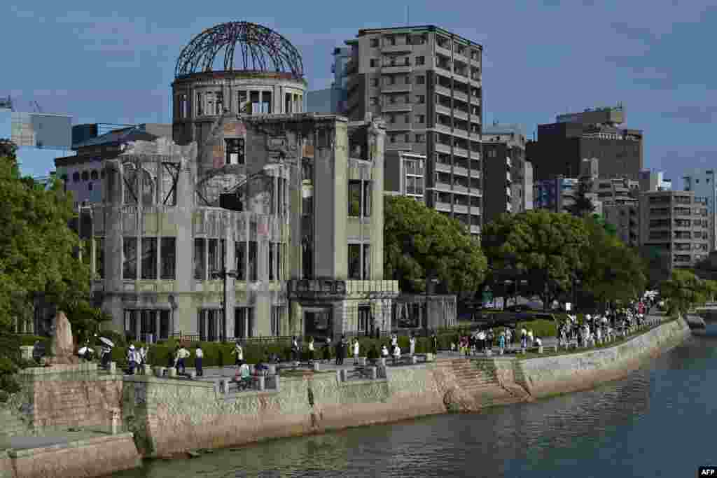 Fotografija 80 godina kasnije prikazuje posjetioce kako prolaze pored istog objekta koji se sada zove Kupola atomske bombe, Hirošima 5. avgust 2025. godine.