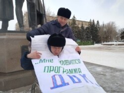 Орынбай Охасов помогает Эрику Жумабаеву надеть плакат перед началом пикета.