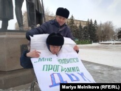 Ерік Жұмабаевқа пикет алдында плакатын тағып алуына Орынбай Оқасов көмектесіп тұр.