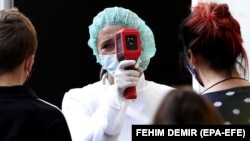 A medical worker measures the body temperature of people arriving for coronavirus testing at a hospital in Sarajevo.