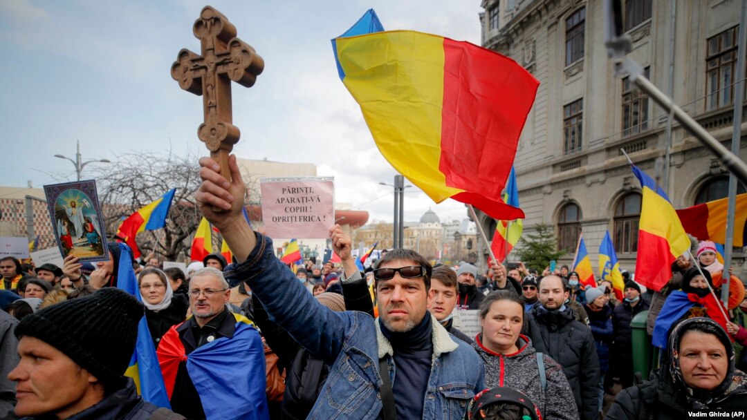 Демонстрант против вакцинација држи дрвен крст додека другите веат национални знамиња за време на протестите во Букурешт во март 2021 година.