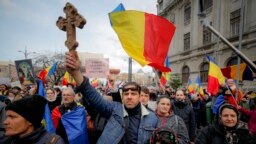 An anti-vaccination protester holds a wooden cross as others wave national flags during a rally in Bucharest in March 2021.