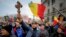 An anti-vaccination protester holds a wooden cross as others wave national flags during a rally in Bucharest in March 2021.