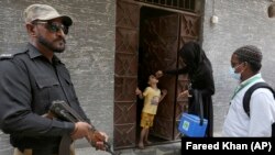 A police officer stands guard while a health-care worker administers a polio vaccine to a child in Karachi, Pakistan, in June. (file photo)