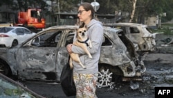 A woman holds her dog as she examines ruins of a car outside a residential building damaged on August 1 during a Russian missile strike.
