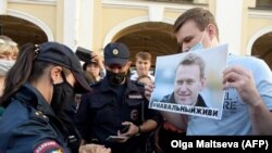 Policajka legitimiše muškarca koji drži plakatu sa likom Aljekseja Navaljnija, opozicionog lidera koji je u bolnici u sibirskom gradu Omsku, na protestu u Sankt Petersburgu. 20. avgust 2020.