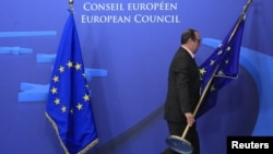 An employee at the EU council in Brussels on November 22 adjusts European Union flags at the entrance of the council headquarters for an EU leaders' summit discussing the bloc's long-term budget.