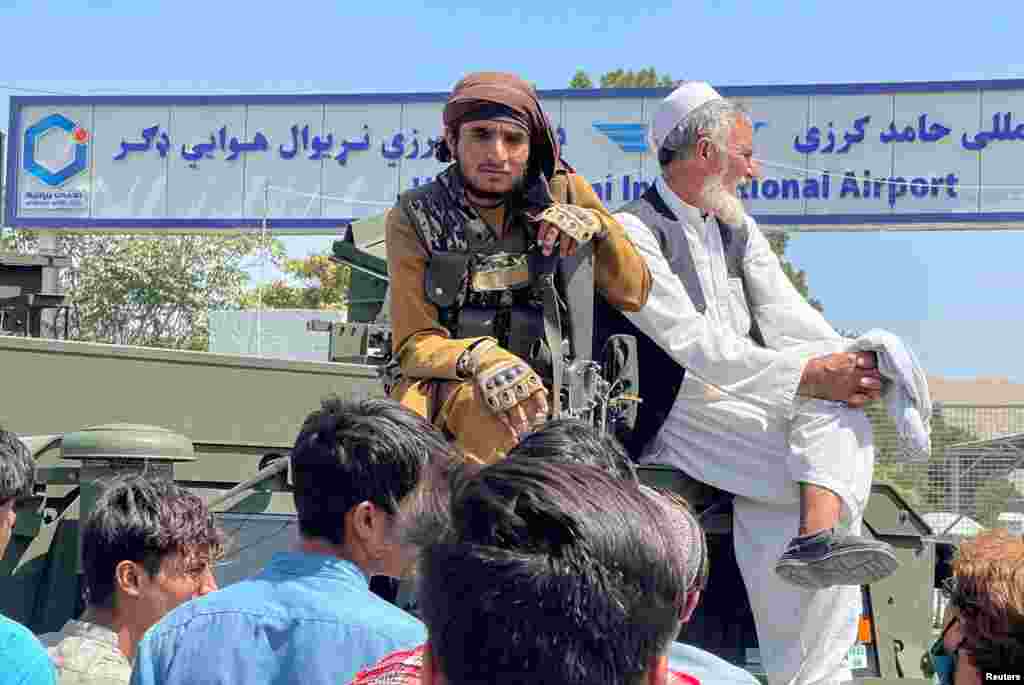 Член на талибанците (лево) седи на оклопно возило и ги набљудува драматичните сцени пред аеродромот во Кабул.