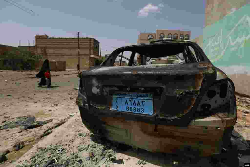 Yemenis walk past the wreckage of a car at the scene of a car bomb a day after it targeted a mosque in Sana'a, on June 18. (epa/Yahya Arhab)