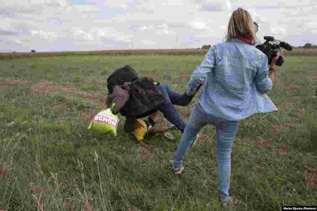 A migrant man carrying a small child falls to the ground after being tripped by TV camerawoman Petra Laszlo while they were trying to escape from a collection point in Roszke, Hungary. Laszlo, who works for a private television channel, was fired after videos of her kicking and tripping migrants spread in the media and on the Internet. (Reuters/Marko Djurica)