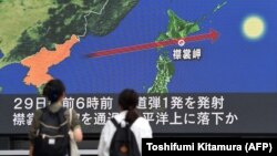 Прохожие на улице разглядывают на большом экране маршрут полета северокорейской ракеты, пролетевшей над японским островом Хоккайдо. Токио, 29 августа 2017 года.