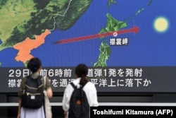 Прохожие на улице разглядывают на большом экране точный маршрут северокорейской ракеты, пролетевшей над Хоккайдо. Токио, 29 августа