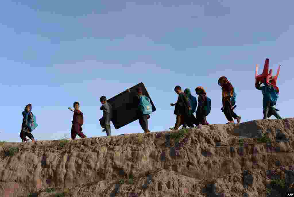 Afghan schoolchildren carry their blackboard and a chair as they walk home after classes at an open-air school outside a brick factory on the outskirts of Jalalabad. (AFP/​Noorullah Shirzada)