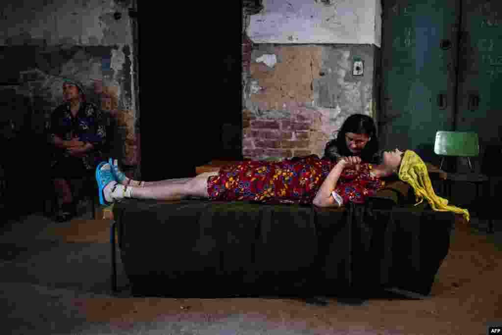 Женщина держит за руку свою больную подругу в подвале бомбоубежища в Донецке.