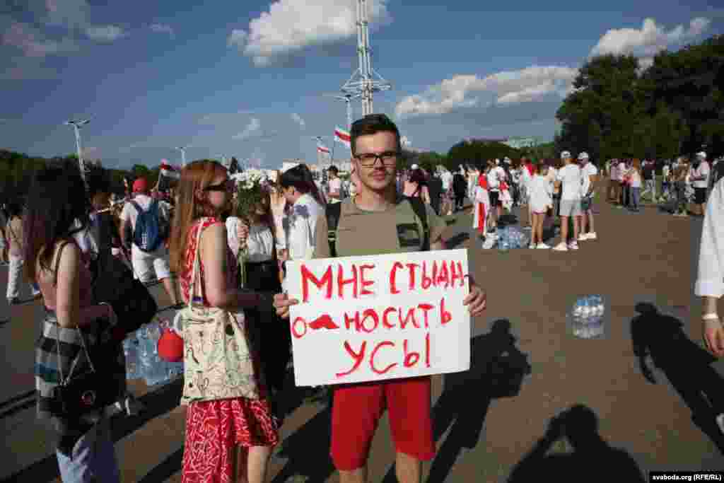 Un manifestant ține un banner pe care scrie : &bdquo;Mi-e rușine să port o mustață&rdquo;, făcând aluzie la podoaba facială a lui Lukașenka.