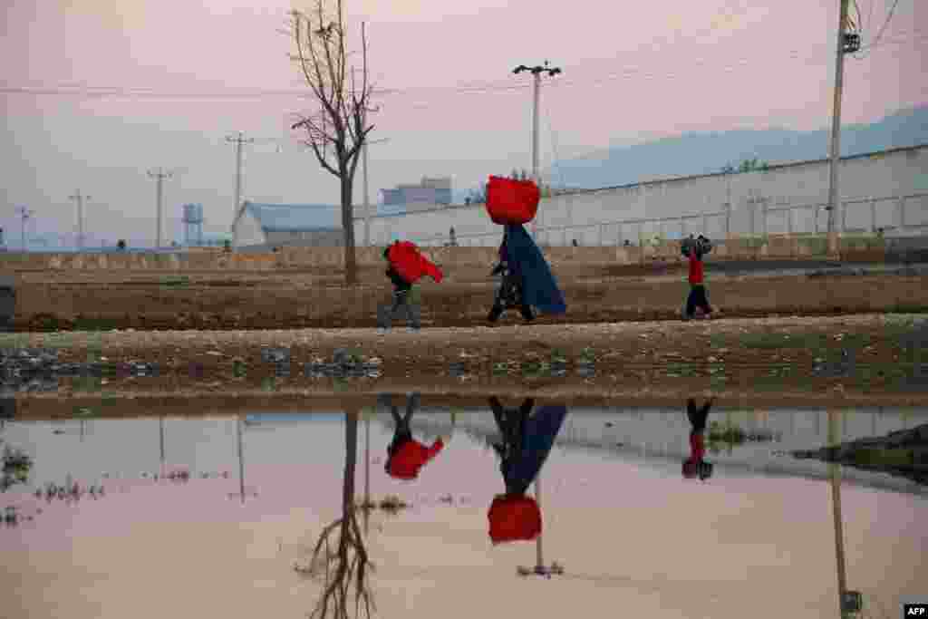 An Afghan woman and her children carry bags on their heads as they walk along a path on the outskirts of Mazar-e Sharif. (AFP/Farshad Usyan)